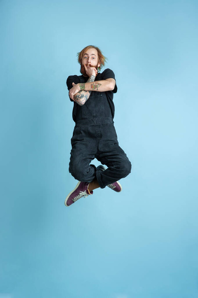 Portrait of young caucasian man looks happy, jumping on blue background - Foto, immagini