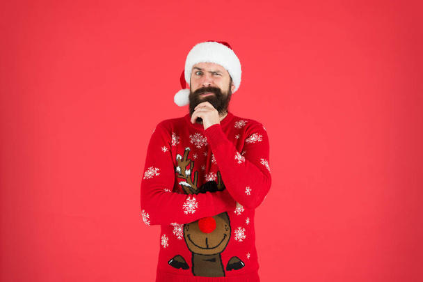 happy new year. cheerful hipster funny knitted sweater. warm clothes in cold winter weather. holiday season mood. bearded man santa hat red background. merry christmas. ready for xmas party - Photo, Image