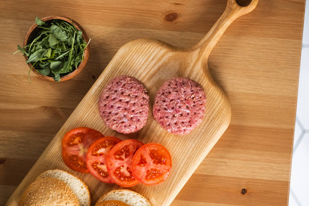 Buns, raw beef cutlets, tomatoes and herbs for burgers cooking. - Foto, imagen