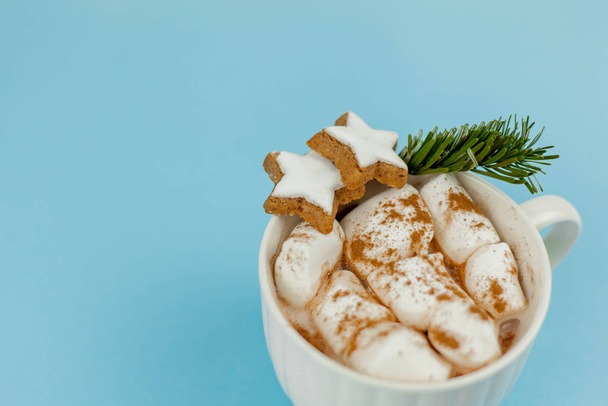 A large white mug with cocoa and marshmallows, cinnamon on a blue background. Christmas cookies. Traditional winter drink. - Photo, Image