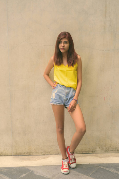 Beautiful teenager girl wearing vibrant yellow shirt against gray background outdoors - 写真・画像