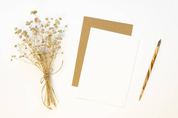 レトロな書道ペンと紙の手紙のクラフトシート白いテーブルの上にドライフラワー冬の花束とモックアップトップビュー - 写真・画像
