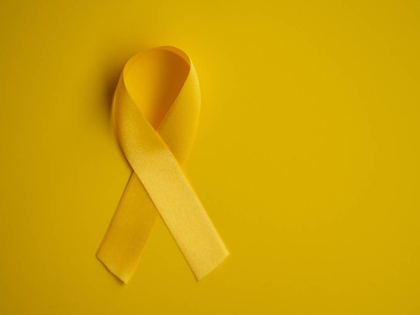 Yellow cancer awareness ribbon on a yellow background. Top view Childhood Cancer Awareness day flat lay - Zdjęcie, obraz
