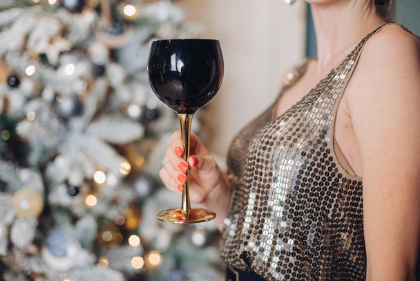 Mano femenina festiva en ropa de fiesta brillante sosteniendo la copa de bebida alcohólica de cerca
 - Foto, imagen