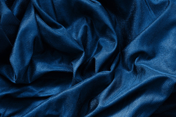 Closeup classic blue macro texture of shiny smooth material fabric or clothing. Toned trendy 2020 year color background with wrinkles and folds. Dark blue monochrome backdrop wallpaper.  - Photo, Image