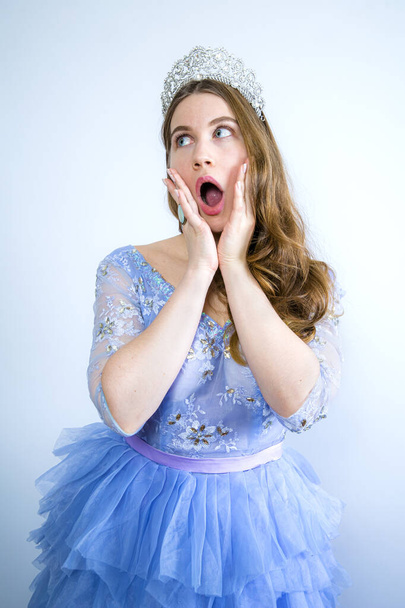 Portrait of a shocked girl wearing crown while looking to the side isolated over light background - Photo, Image