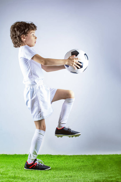 Full profile length shot of a little soccer player juggling a football isolated on gray background - Foto, imagen
