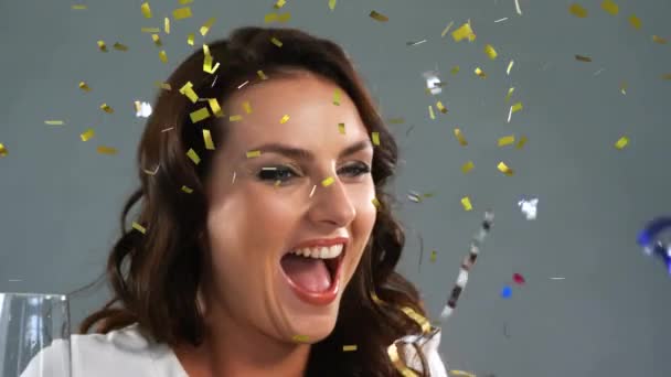 Animation of young Caucasian woman holding a glass of champagne, celebrating and laughing with golden confetti falling on grey background - Metraje, vídeo