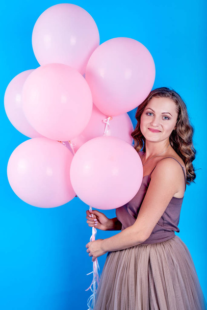 Happy smiling young woman in dress holding pink helium air balloons over blue background - Foto, Imagem