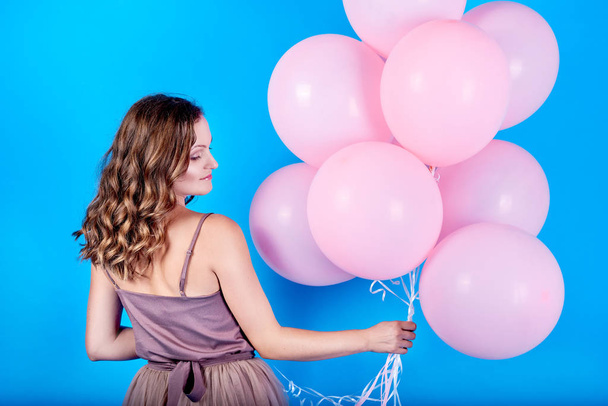 Beautiful young woman in dress holding pink balloons over blue background - Фото, изображение