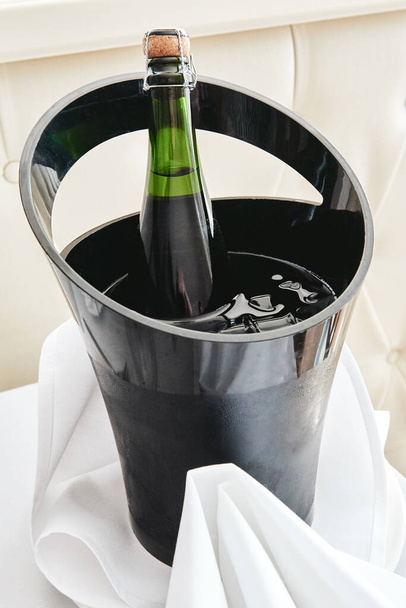 Μπουκάλι κρύο κρασί ή σαμπάνια σε κουβά πάγου στο λευκό τραπέζι στο - Φωτογραφία, εικόνα