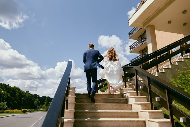 Happy bride and groom dancing walking up the stairs in hotel at wedding day - 写真・画像