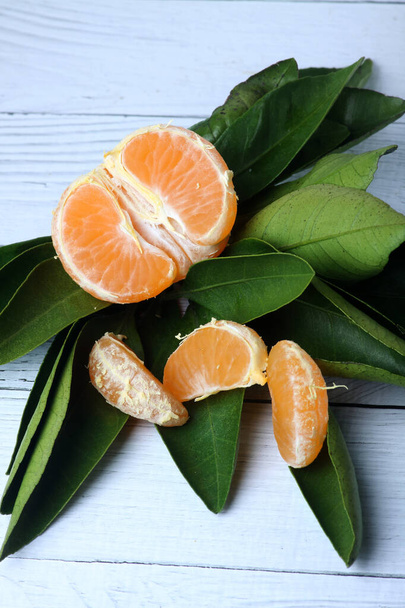 half of peeled tangerine and green leaves isolated on wooden white background. vertical picture. - 写真・画像