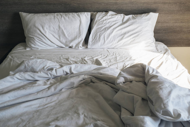 White pillow and blanket on bed unmade. Messy bed after used . wrinkled white bed, pillow and bedsheets - Φωτογραφία, εικόνα
