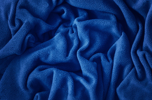 Nahaufnahme klassische blaue Makrotextur aus blauem Fleece-Material Stoff oder Kleidung. getönte trendige 2020 Jahr Farbe Hintergrund mit Falten und Falten. dunkelblau monochromen Hintergrund Tapete.  - Foto, Bild
