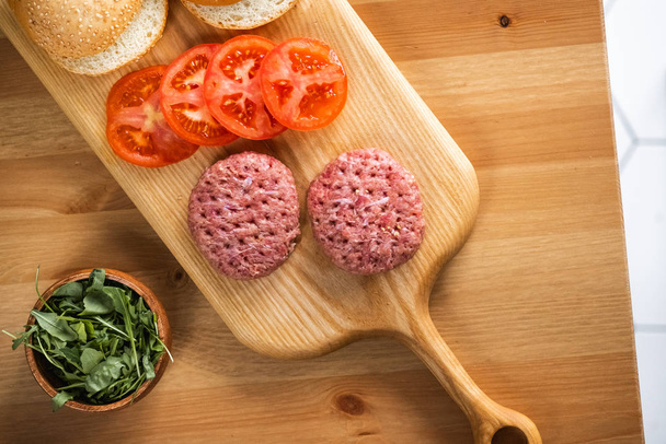Brötchen, rohe Rinderschnitzel, Tomaten und Kräuter zum Kochen von Burgern. - Foto, Bild
