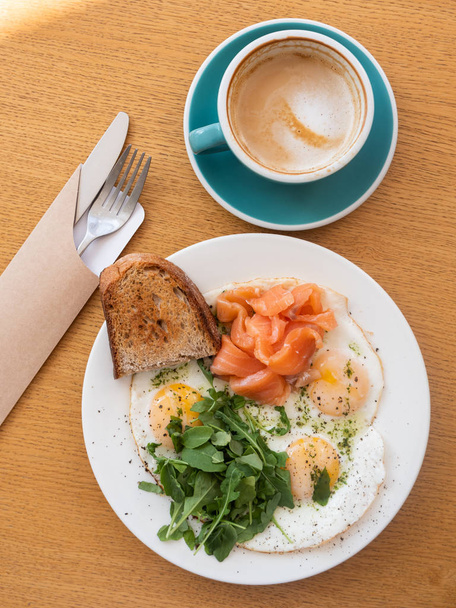 Fried eggs served with salmon, bread, arugula on table with coffee latte - Foto, immagini