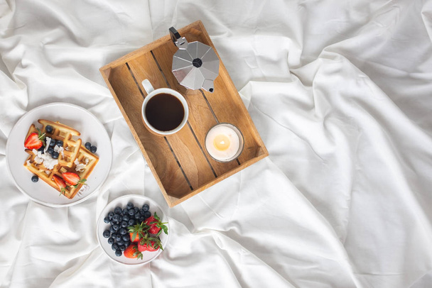 Поднос с кофе, ягодами и вафлями подается на кровати
. - Фото, изображение