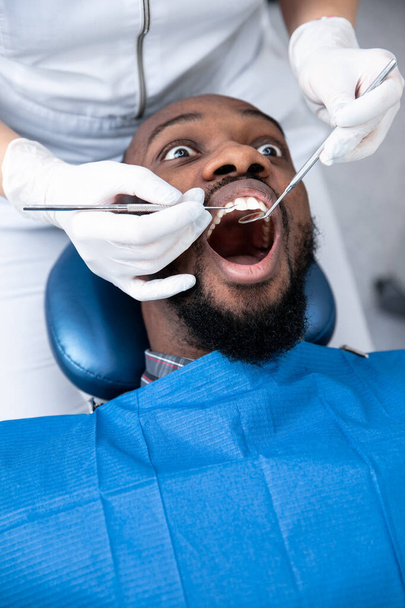 Young african-american man visiting dentists office, looks scared - Foto, afbeelding