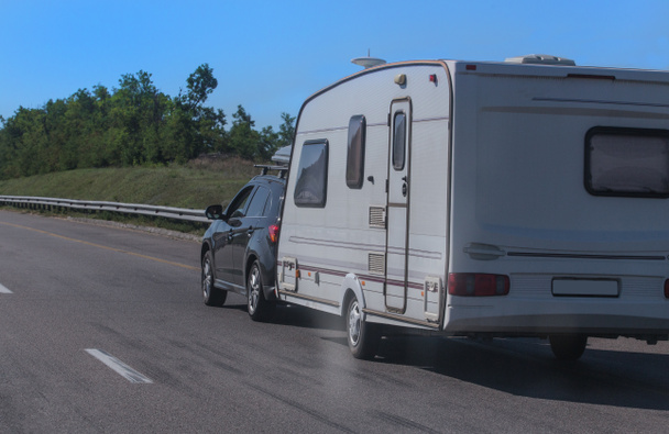 SUV com um trailer de acampamento está se movendo ao longo da estrada
 - Foto, Imagem