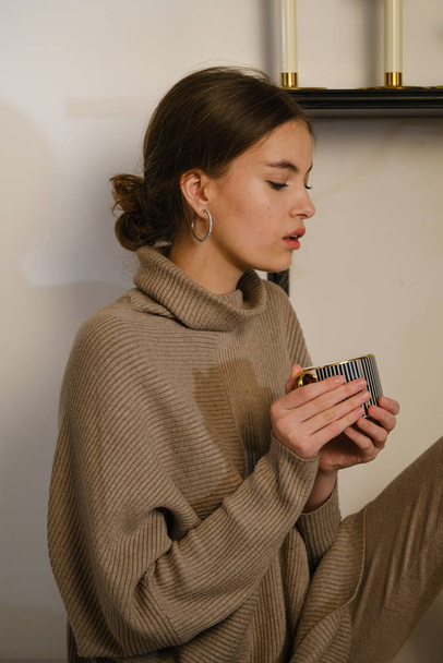 Pretty woman in brown knitted sweater holding cup in hands - Foto, Imagem