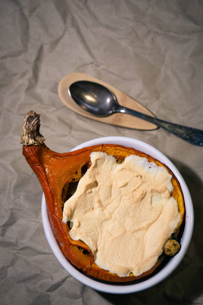 Citrouille Hokkaido cuite au four avec meringue au milieu. Nature morte avec légumes cuits à l'orange et cuillère à dessert sur papier sombre froissé
. - Photo, image