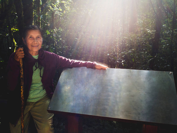 Senior vrouw met een wandelstok reizen door een bos handen geplaatst op blanco stalen bord - Foto, afbeelding