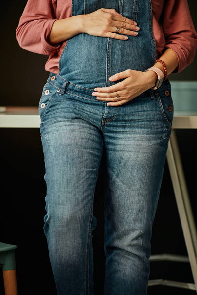 Крупним планом кавказька вагітна жінка стоїть в домашньому офісі, спираючись на стіл і зворушливий живіт
. - Фото, зображення