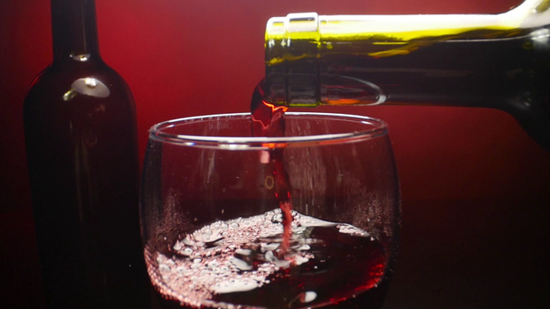 Red wine pouring into a wine glass on red background in slow motion - Séquence, vidéo