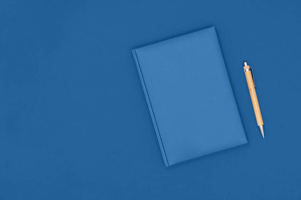 Jegyzetfüzet és toll kék háttérrel. Üzleti koncepció. Felülnézet, lapos fekvés, másolás. Az év trendi színe 2020. - Fotó, kép