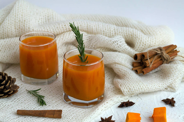 cocktail with sprig of rosemary and sticks of cinnamon on the warm white plaid on white table. two glasses of fresh pumpkin or oranges juice with slices of pumpkin, spices and winter decoration. - 写真・画像