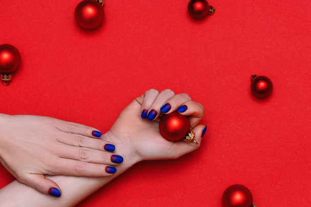 Kobieta ręce z modnym manicure gospodarstwa Christmas zabawki na czerwonym tle. - Zdjęcie, obraz