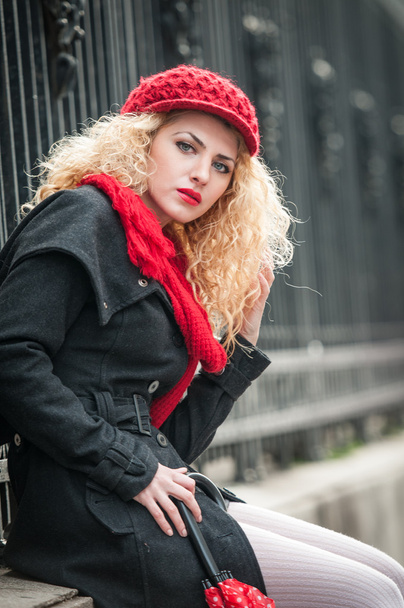 Attractive young woman in a winter fashion shot. Beautiful fashionable young girl with red umbrella in the street - Fotoğraf, Görsel