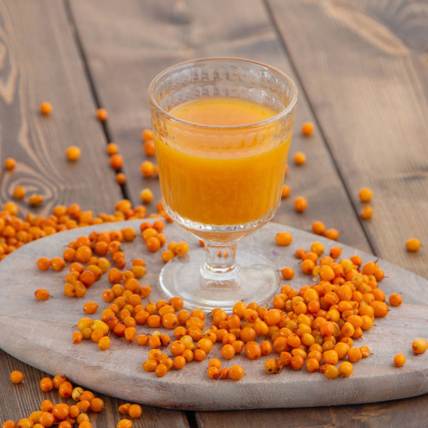 sea buckthorn of the morse in a beautiful glass on a wooden background of berries scattered - Foto, imagen