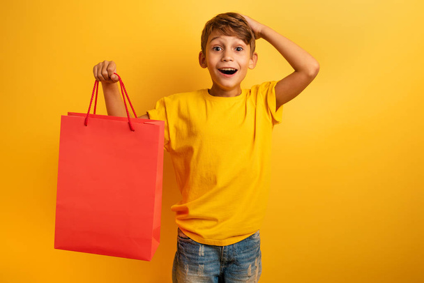 Ευτυχισμένο παιδί είναι κατάπληκτοι με τις πωλήσεις των καταστημάτων. Έκπληξη, έκφραση. Κίτρινο χρώμα φόντου - Φωτογραφία, εικόνα