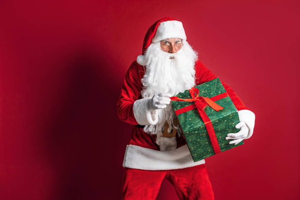 Photo of kind Santa Claus giving xmas present and looking at camera - Foto, Imagen
