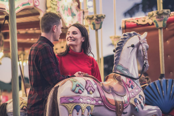 romantic couple taking a moment to kiss while riding horses on carousel - Photo, image