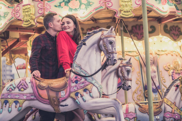 romantic couple taking a moment to kiss while riding horses on carousel - Fotó, kép