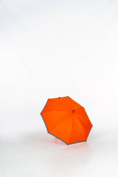 Egy nyitott narancssárga esernyő szürke szélekkel egy fotóstúdióban, fehér háttérrel. Elszigetelt fehér háttér, hely a szövegnek. - Fotó, kép
