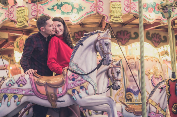 romantic couple taking a moment to kiss while riding horses on carousel - Fotoğraf, Görsel
