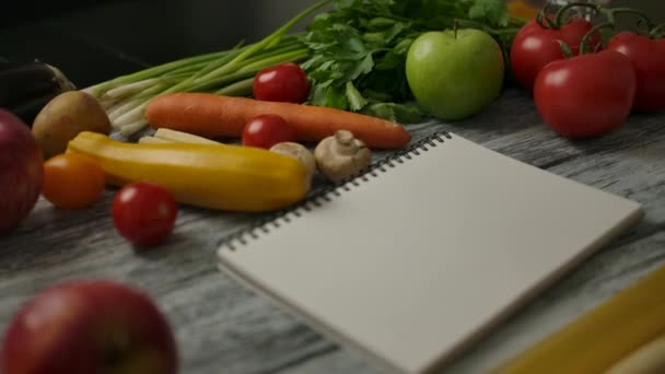 Bloc de notas en blanco para la receta en medio de la comida vegana en la mesa - Metraje, vídeo