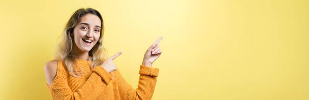 young beautiful woman wearing yellow sweater and glasses pointing to the side with a confident smile on the camera. - Foto, Imagen