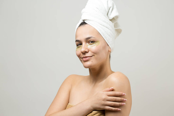 Young beautiful girl in a white towel on his head wears collagen gel patches under her eyes. Mask under eyes treatment face. - Fotografie, Obrázek