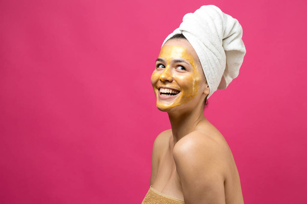 Retrato de belleza de mujer en toalla blanca en la cabeza con máscara nutritiva de oro en la cara. Limpieza de la piel ecológico cosmético spa relajante concepto
. - Foto, imagen