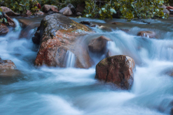 Nature scene of rough, fast flowing river hitting the stones, making mini waterfalls. - Photo, Image
