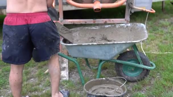 Młody pracownik zbiera roztwór betonu z taczki do wiadra - Materiał filmowy, wideo