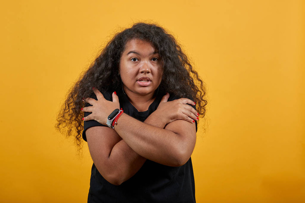 Joven afroamericana con sobrepeso abrazándose, manteniendo las manos cruzadas
 - Foto, imagen