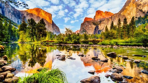 Sunset glow over El Capitan on the left and Cathedral Rocks, Sentinel Rock and Bridalveil Fall on the right and reflecting in the calm water of Merced River in Yosemite National Park, California, USA - 写真・画像