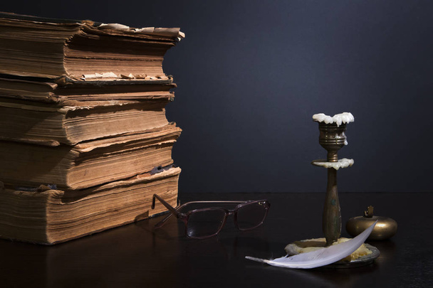 Στοίβα αρχαίων βιβλίων με κιτρινισμένες σελίδες, γυαλιά, κηροπήγιο με καμένο κερί και μικρό χάλκινο τασάκι τσέπης - Φωτογραφία, εικόνα