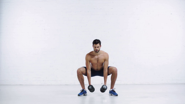sportsman squatting with dumbbells on white background - Πλάνα, βίντεο